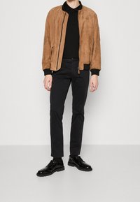 Suede tan bomber jacket, black polo shirt, navy pants, and black lace-up shoes with textured soles. Simple design, no prominent patterns.