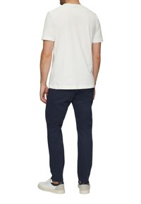 Witte katoenen T-shirt gecombineerd met marineblauwe chinos. De outfit heeft een ronde halsontwerp en wordt aangevuld met lichte sneakers.