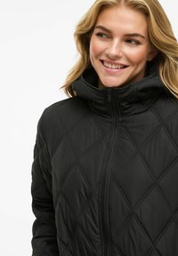 Black quilted jacket with high collar and zip closure. Features a diamond pattern and lightweight, padded material for warmth.