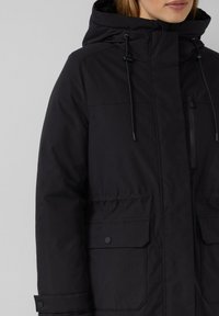 Schwarze isolierte Jacke mit Kapuze, Kordelzügen, frontalen Taschen und einer glatten Oberflächenstruktur. Mittellanges Design mit funktionalem Akzenten.