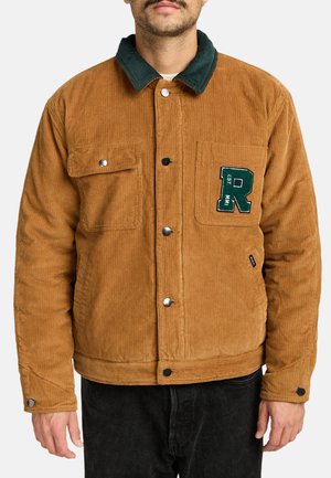 Man draagt een bruine corduroy jas met groene kraag, zilveren drukknopen en een groene letter R patch op de borstzak.