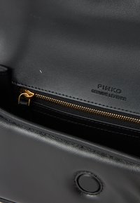 Vnútro čiernej koženej kabelky so zlatým zipsom, s embosovaným textom "PINKO GENUINE LEATHER" a hladkou textúrou.