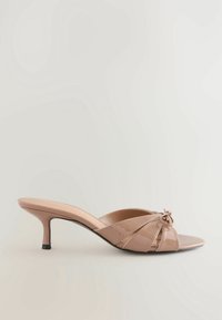Mule en cuir verni beige avec un petit talon kitten et des brides nouées sur un bout ouvert.