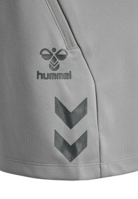 Grijze stof met een ritsdetail, voorzien van het zwarte Hummel-logo en twee naar beneden wijzende chevronstrepen op het onderste gedeelte.