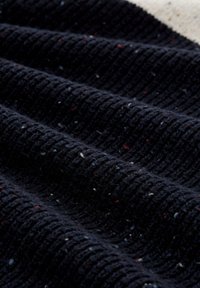 Dunkelblaues, geripptes Strickgewebe mit kleinen roten, weißen und blauen Farbklecksen, nah aufgenommen mit texturierten Falten und Schatten.