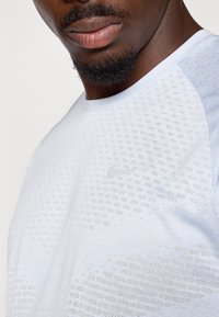 Tricou sportiv de culoare albastru deschis, cu un model texturat și mâneci raglan. Prezintă un logo subtil în zona pieptului. Material moale.