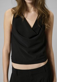 Black sleeveless top with a cowl neckline, made from a smooth fabric, featuring a fitted design and a cropped length.