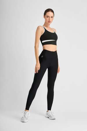 Black sports bra with white accents and high-waisted black leggings. Model wears white athletic shoes. Smooth, fitted fabric. Simple design.