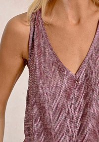 Top in tessuto strutturato rosa con scollatura a V, caratterizzato da un motivo ondulato e una lucentezza evidente; il design senza maniche esalta le spalle.
