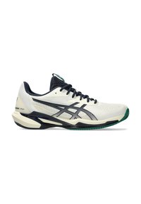 Lichte atletische schoen met een witte mesh bovenkant, donkerblauwe accenten en een groene rubberen zool. Heeft een slank ontwerp met zichtbare stiksels.