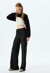 Zwarte cropped sweatshirt met een beige paneel, gecombineerd met brede, zwarte ribgebreide broek. De outfit heeft een relaxed fit en een taille met koord.