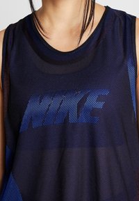 Canotta sportiva Nike in rete blu scuro, con un grande logo azzurro. Design senza maniche con scollatura rotonda e tessuto testurizzato.