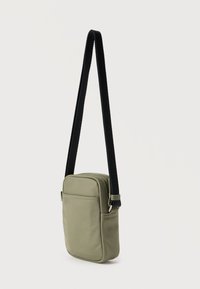 Τσάντα χιαστί ελιάς από λείο ύφασμα, με ορθογώνιο σχήμα, ρυθμιζόμενο μαύρο λουρί και μπροστινή τσέπη με φερμουάρ.