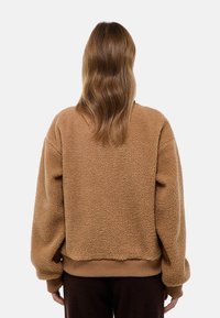 Pull en polaire brun avec une surface douce et texturée, coupe oversize, poignets et ourlet côtelés. Vue de dos, sans graphiques ni motifs visibles.