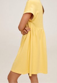 Vestido amarillo de manga corta con cintura plisada, corte hasta la rodilla, tejido suave de algodón y una silueta relajada.