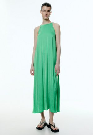 Grünes ärmelloses Maxikleid aus leichtem Material, mit lockerer Passform und A-Linien-Silhouette, kombiniert mit schwarzen Flip-Flops.