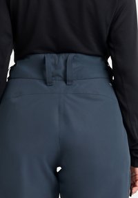 Hochtaillierte marineblaue Hose aus einem glatten, dehnbaren Material; verfügt über eine mittige hintere Naht und zwei horizontale Gürtelschlaufen.