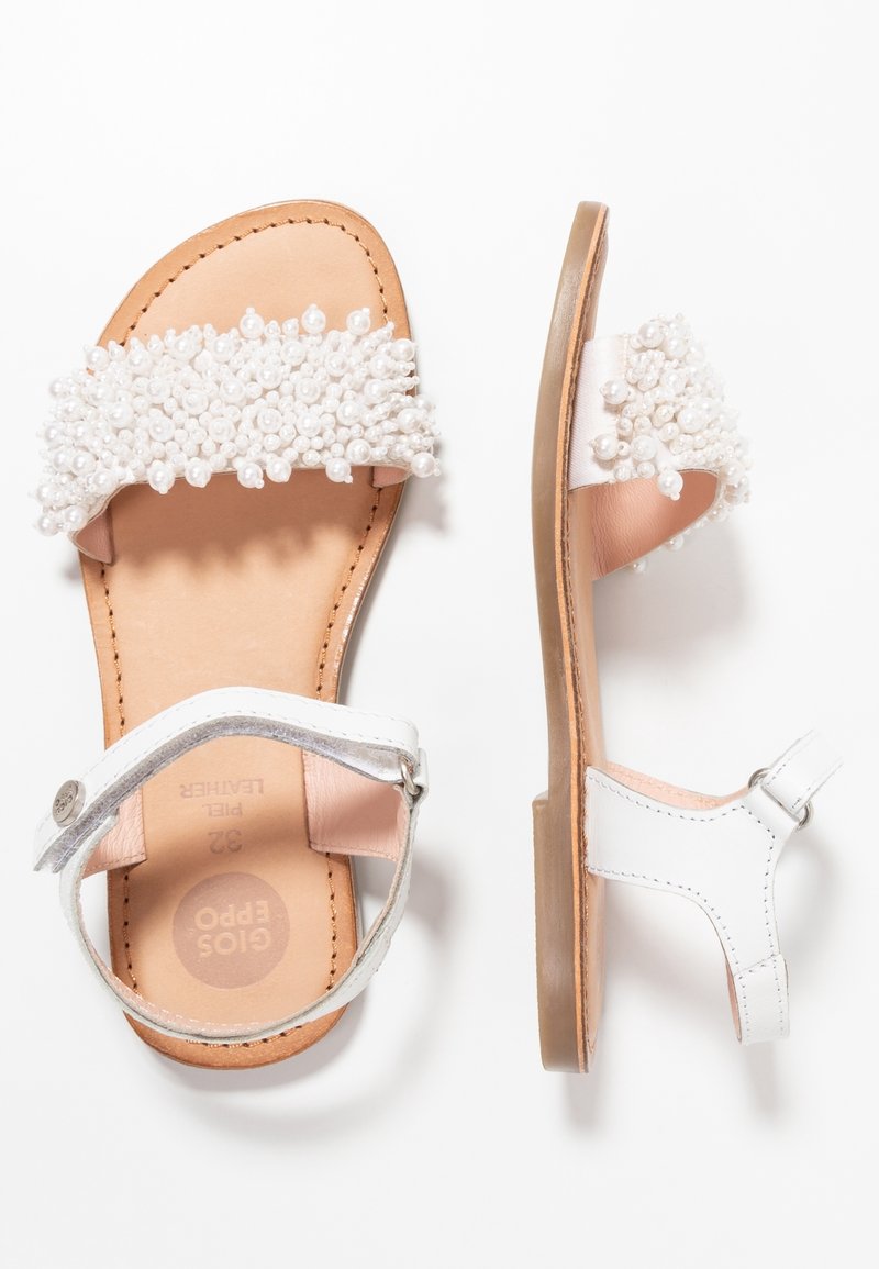 Sandales plates en cuir blanc avec brides à la cheville et à l’avant, ornées de grappes de petites perles blanches.