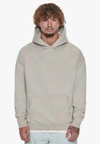 Beige hoodie med kængurulomme, ribbede manchetter og kant. Har et lille præget logo på forsiden. Blød, glat tekstur.