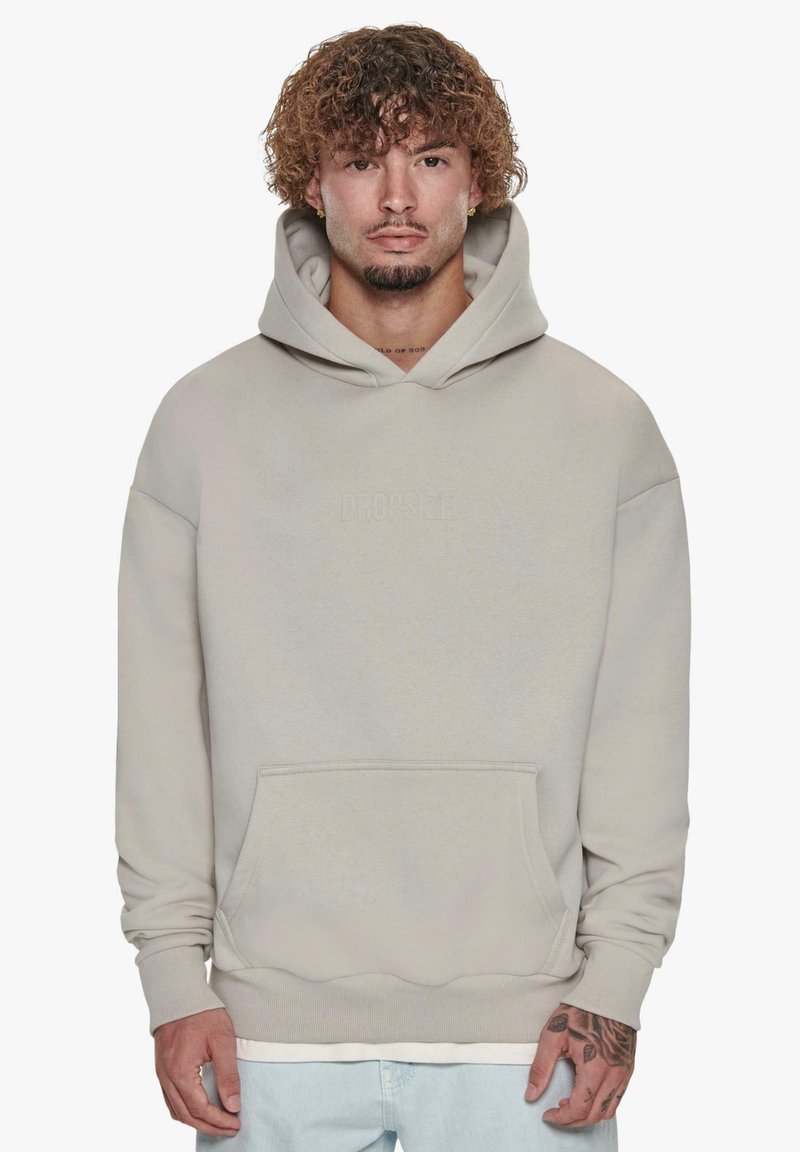Beige hoodie med kængurulomme, ribbede manchetter og kant. Har et lille præget logo på forsiden. Blød, glat tekstur.