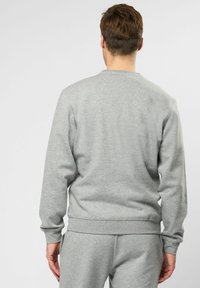 Světlé šedé crewneck mikina vyrobená z měkkého materiálu, s žebrovanými manžetami a lemem, s minimalistickým designem a bez viditelných log.