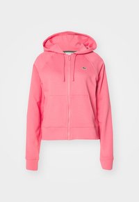 Sweat à capuche rose avec fermeture éclair, poches avant, capuche avec cordon, manches longues, poignets côtelés et un petit logo crocodile vert sur la poitrine.