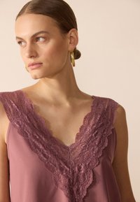 Top sin mangas de escote en V profundo en color malva, con borde de encaje floral en el cuello. Tejido suave con una textura delicada y un diseño minimalista.