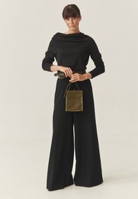 Zwart top met lange mouwen en een gedrapeerde halslijn, ruime zwarte broek, en een kleine oliën groene leren handtas. Gladde stof en ontspannen pasvorm.