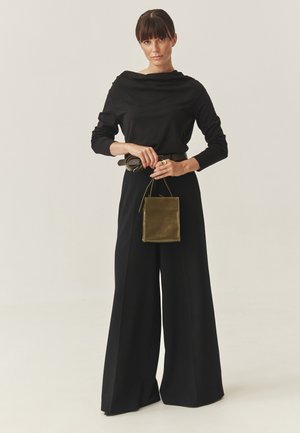 Crna majica s dugim rukavima i preklopnim izrezom, široke crne hlače i mala kožna torbica maslinasto zelene boje. Glatki materijal i opušteni kroj.