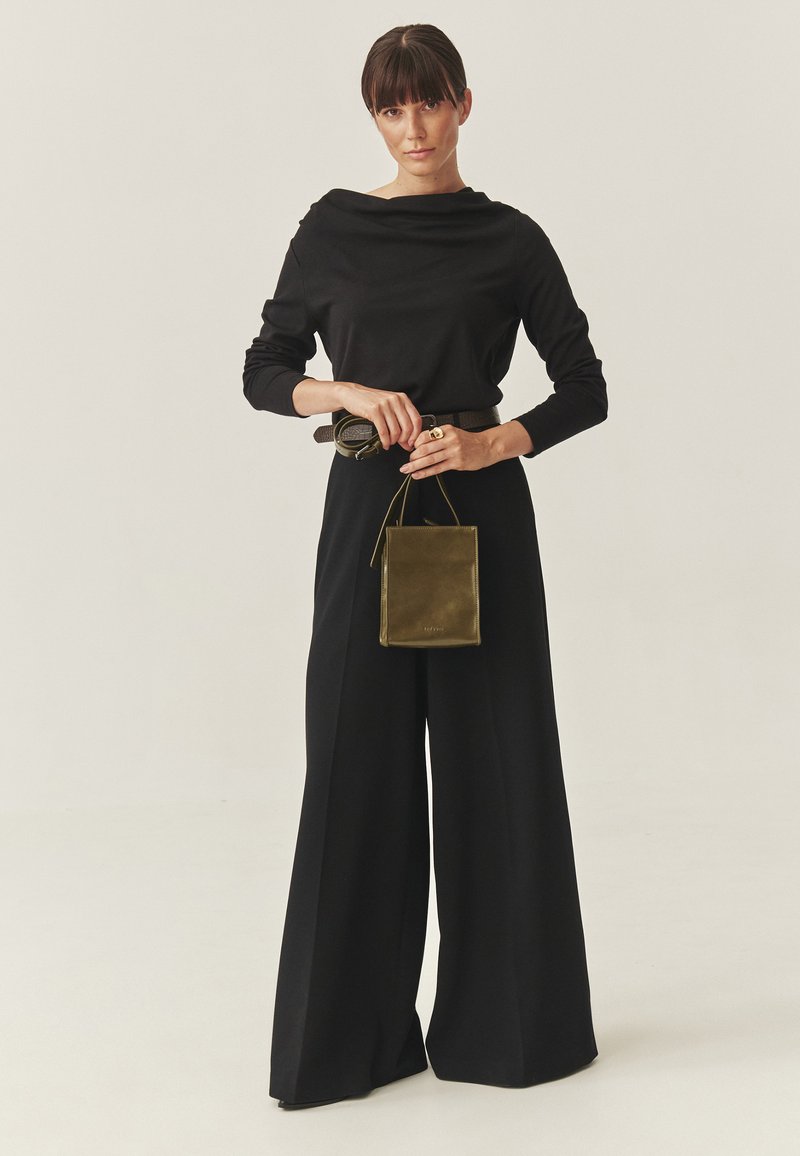 Zwart top met lange mouwen en een gedrapeerde halslijn, ruime zwarte broek, en een kleine oliën groene leren handtas. Gladde stof en ontspannen pasvorm.