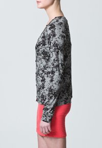 Šedé tričko s dlouhým rukávem s černým skvrnitým vzorem, ve spojení s lososově korálovou sukní; má výstřih do V a přiléhavý střih.