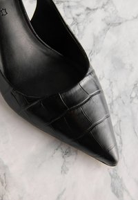 Melnas garās pirkstu kurpes, izgatavotas no teksturēta lakotā āda ar krokodila rakstu un elegantu, minimālistisku dizainu.