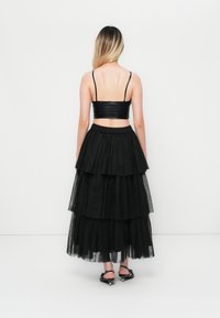 Schwarzes Zweiteiler-Outfit mit einem enganliegenden, glänzenden Cropped-Top mit dünnen Trägern und einem geschichteten, gestuften Tüll-Maxirock mit elastischem Bund.