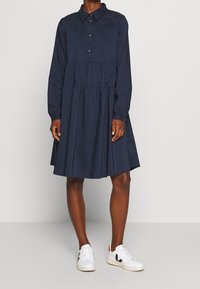 Mörkblå knapplång klänning med långa ärmar, rynkad midja och utsvängd kjol. Tillverkad av ett mjukt, lättviktigt tyg.