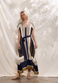 Abito lungo e fluente con scollo a V, maniche a cappuccio e cintura annodata in vita. Il tessuto presenta audaci strisce geometriche nei colori blu navy, bianco e oro.