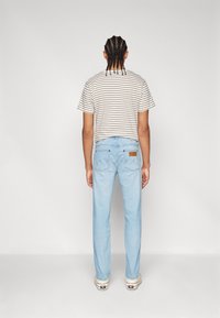 Lichtblauwe denim jeans met een rechte pijp, gecombineerd met een beige en witte gestreepte t-shirt. Zichtbare stiksels en twee achterzakken.