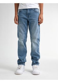 Vaqueros de mezclilla azul claro con un corte relajado, acentos desgastados, diseño de cinco bolsillos y detalles de costura sutiles, combinados con zapatillas blancas.
