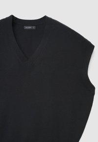 Schwarzer ärmelloser Pullover mit V-Ausschnitt und geripptem Saum; weiche Textur; minimalistisches Design; Etikett am Halsausschnitt sichtbar.