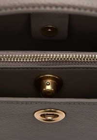 Unutra sive kožne torbice nalazi se zlatni metalni zatvarač, kopča i teksturirana podstava. Ima glatku površinu i minimalistički dizajn.