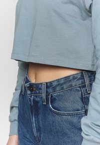 Felpa corta azzurro chiaro con maniche lunghe e orlo grezzo, abbinata a jeans in denim blu scuro a vita alta con chiusura a bottone e tasche.