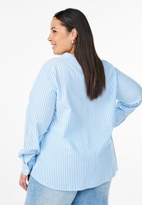 Camicia button-up a righe blu chiaro e bianca, maniche lunghe, vestibilità casual, orlo curvo, abbinata a jeans blu chiaro.