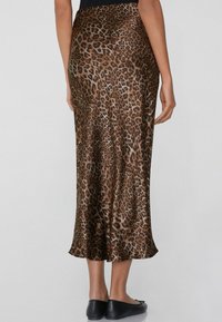 Jupe imprimée léopard en tissu lisse, mi-longue, avec une taille ajustée et une silhouette fluide, associée à des ballerines noires simples.