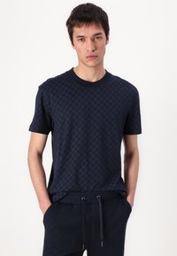 Camiseta de manga corta azul marino en tejido texturizado con un sutil patrón geométrico. Cuello redondo y corte relajado. Combinada con pantalones oscuros a juego.