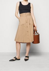 Tans A-lijn rok met een riem taille, knoopsluiting aan de voorkant en zijzakken. Gepaard met zwarte muilen en een bruine leren emmer tas.