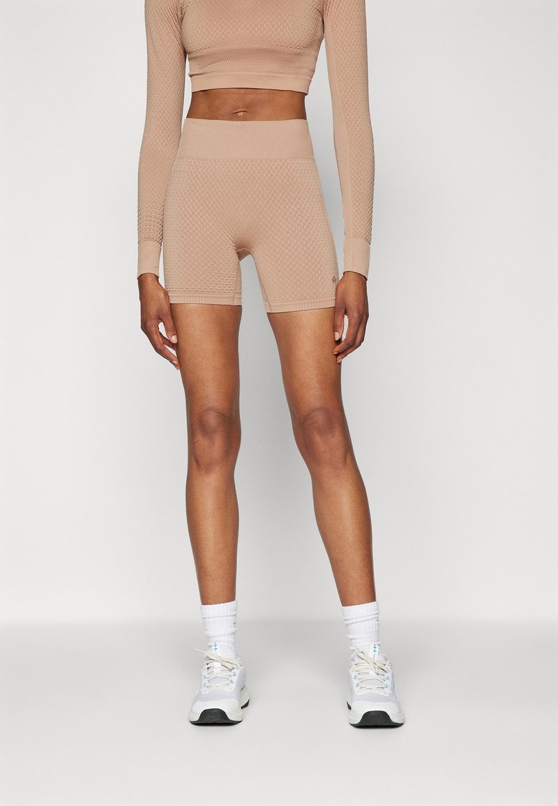 Personne mince portant un crop top beige texturé à manches longues et un short cycliste taille haute assorti, avec des chaussettes blanches et des baskets blanches.