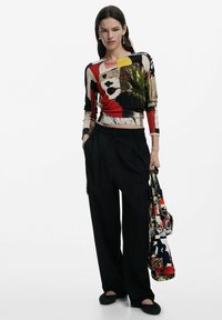 Top a maniche lunghe con un motivo multicolore e un design grafico; pantaloni neri a vita alta; scarpe flat nere; borsa con stampe vivaci.