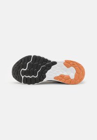 Suela de una zapatilla deportiva con almohadillas de tracción de goma texturizada en negro, blanco y naranja sobre una base blanca.
