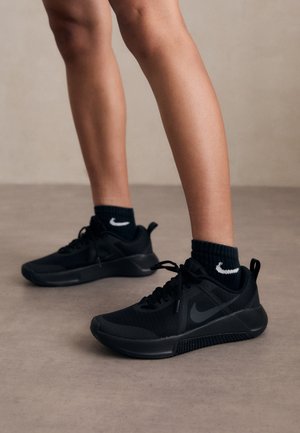 Gros plan de jambes portant des baskets Nike noires et des chaussettes noires avec le logo blanc Nike sur un sol gris lisse.