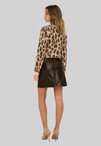 Suéter estampado en tonos beige y marrón, combinado con una falda de cuero sintético negra. El conjunto presenta una silueta ajustada y mangas largas.