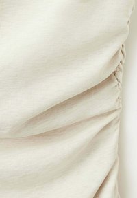 Gros plan sur un tissu côtelé beige avec un détail élastique froncé sur un côté, créant des plis doux et de la texture.